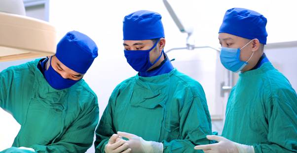 The image shows three medical professionals, all wearing blue surgical gowns and masks, engaged in a medical procedure, possibly in an operating room.

AI-generated content may be incorrect.